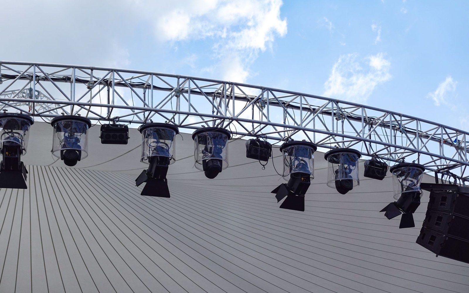 Stage lighting rig with speakers mounted on a curved metal truss under a tented roof