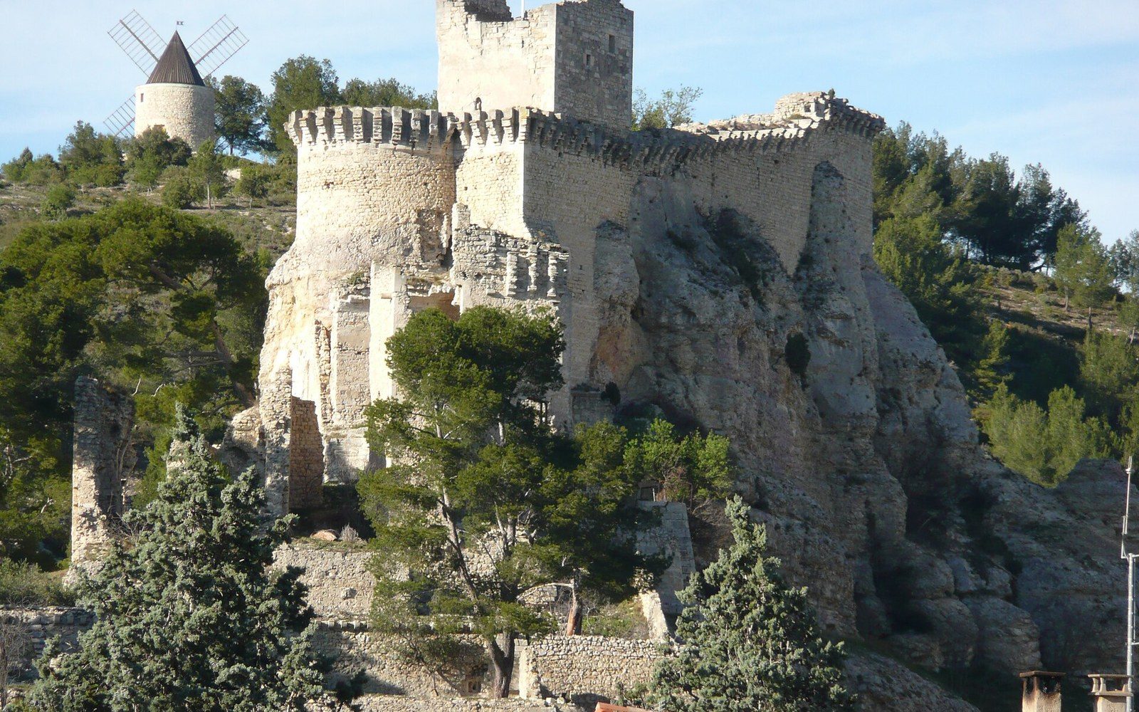 Ruined stone castle with round turrets perched atop a rocky cliff beside a windmill
