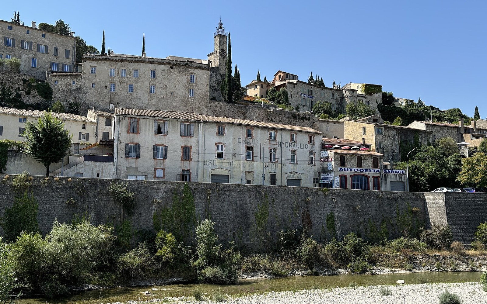 Hillside town of Vaison-la-Romaine rises above a stone riverbank wall and the Ouvèze river